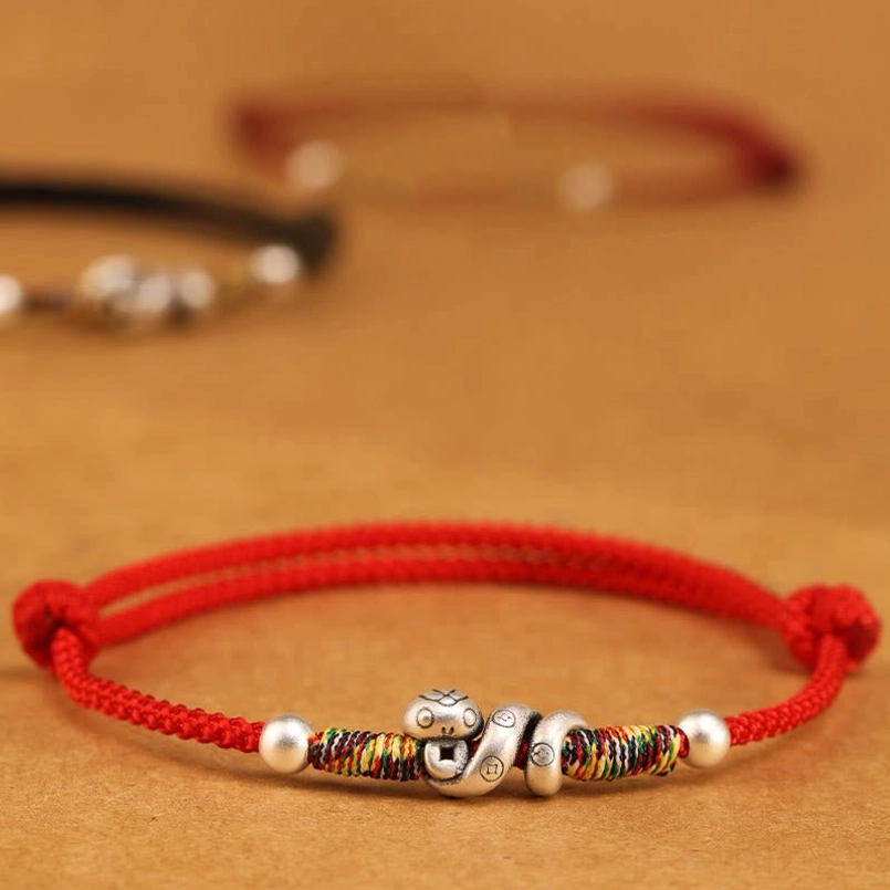 Flat lay of Year of the Snake sterling silver anklet on wooden surface showing adjustable knot, silver snake charm, and full design details