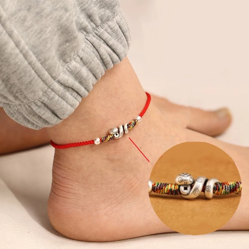 Year of the Snake sterling silver red string anklet worn on ankle, side view showing woven red cord with silver snake charm and colorful beaded details