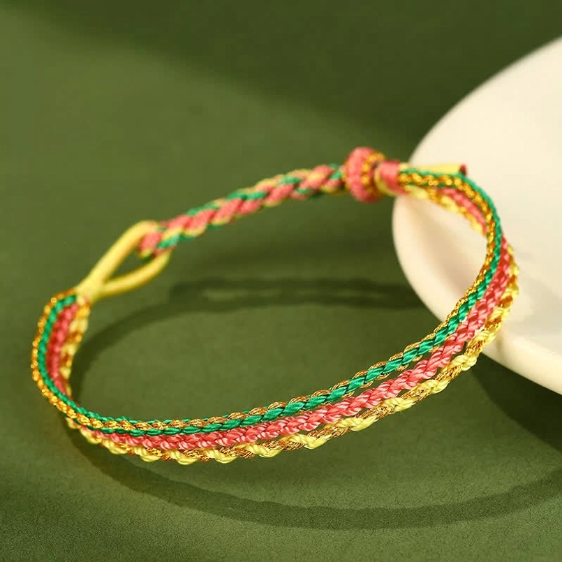 Yellow pink and green triple wrap braided cord bracelet laid flat on green background with ceramic dish