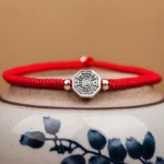 Yin Yang Bagua cinnabar red string bracelet with sterling silver charm on blue ceramic backdrop