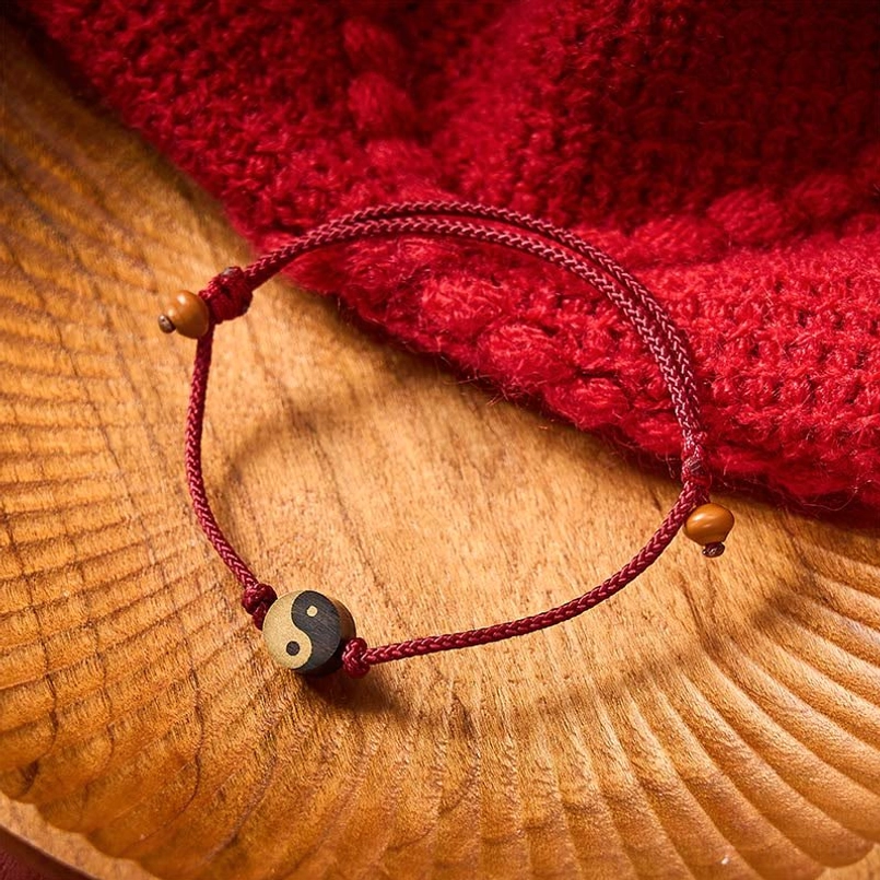 Yin Yang wooden charm detail on red braided cord with brown accent beads