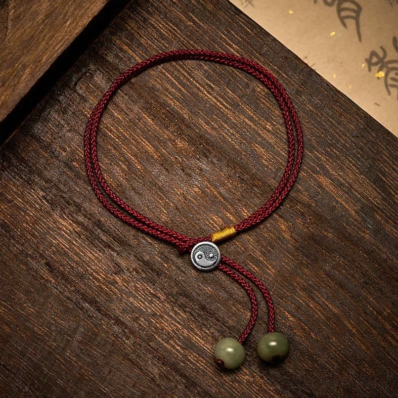 Flat lay view of handmade Yin Yang protection bracelet with braided wine-red cord and silver charm
