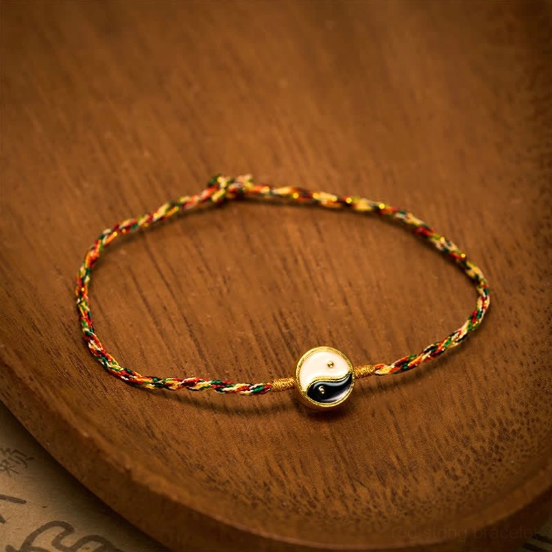Flat lay of multicolor braided red string bracelet with metal-trimmed Yin Yang bead on wooden tray