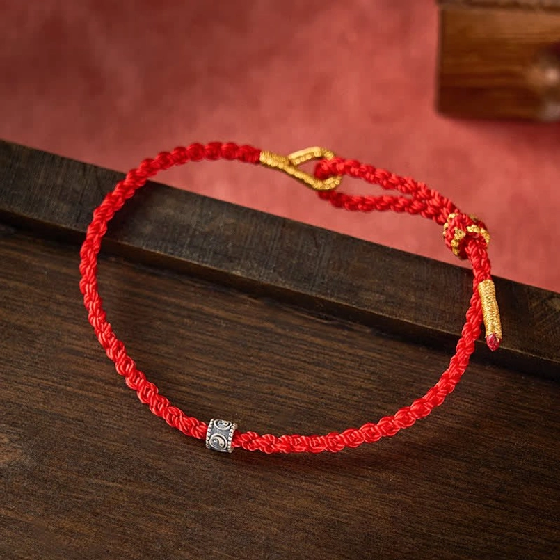 Hand-woven red cord bracelet with silver Yin Yang bead and gold adjuster on dark wood