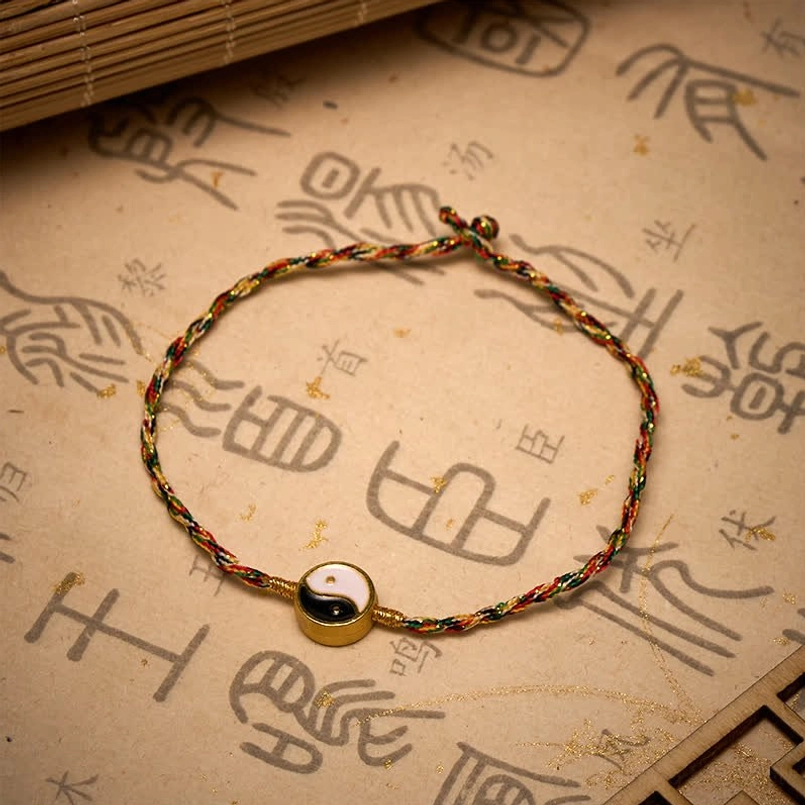Hand-woven colorful red string bracelet with metal-framed Yin Yang bead on ancient Chinese character paper