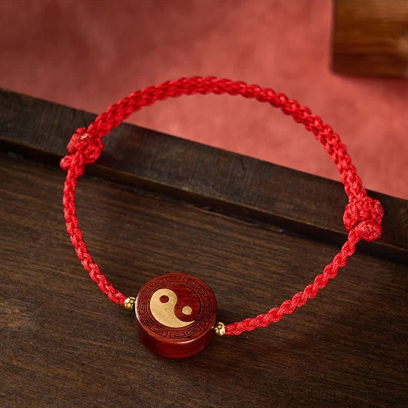 Tai chi wooden charm with engraved border and gold inlay on braided red cord, side angle view