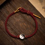Handwoven Yin Yang red string bracelet with silver charm and gold adjustable ends on dark wood