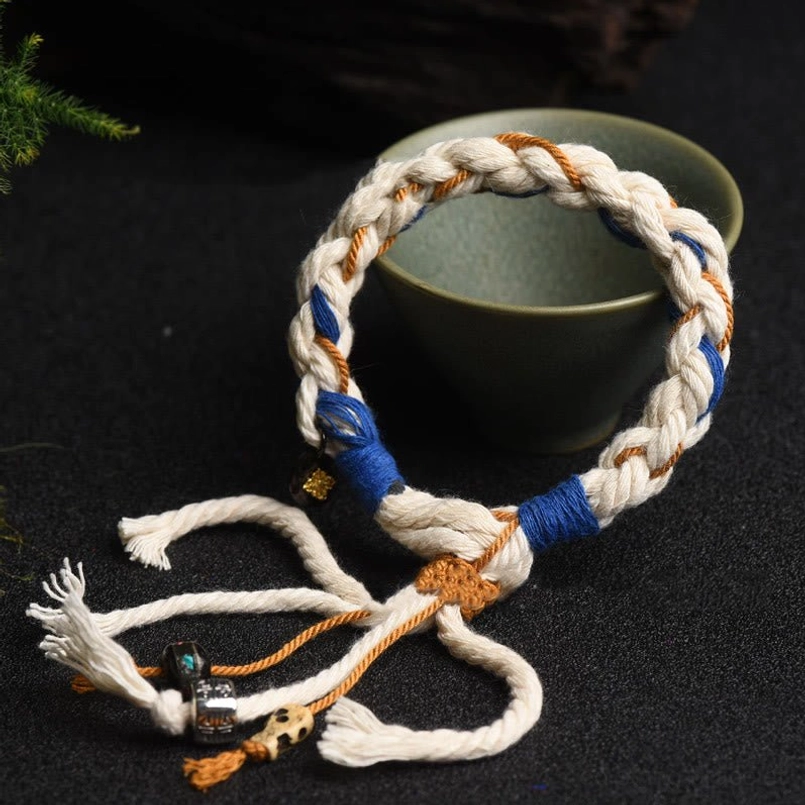 Tibetan red string luck bracelet with braided cord and mixed metal stone charms displayed with green ceramic bowl