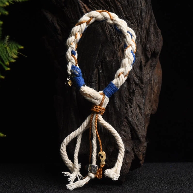 Vertical hanging display of red string Zakiram bracelet showing twisted rope and small hanging charms against wood