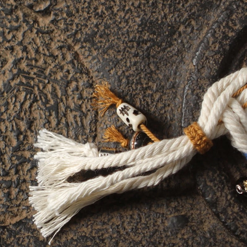 Top-down close-up of Zakiram red string bracelet showing white braided rope, brown knot and decorative charm detail