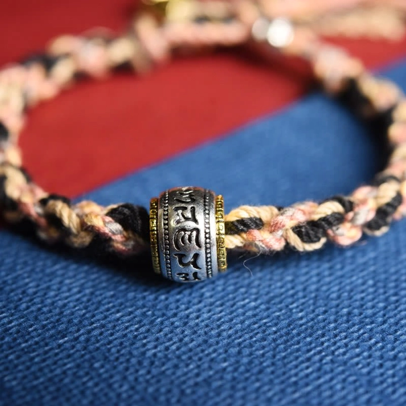 Close-up detail of Sanskrit inscribed rotating metal bead on Zakiram red string bracelet