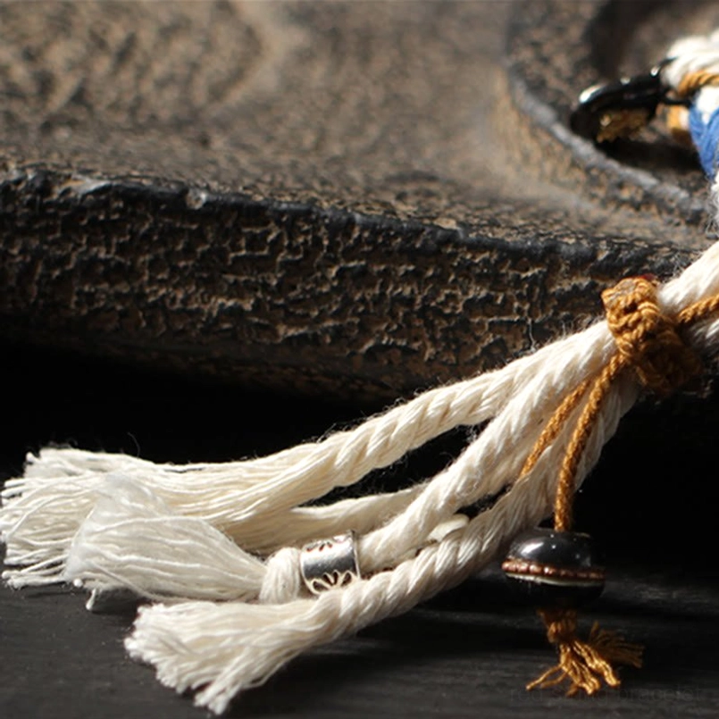 Macro detail of handcrafted Zakiram bracelet with brown binding knot and multiple tassel strands with metal accent