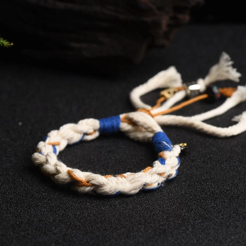 Top-down view of compact handmade Zakiram Goddess bracelet with tri-color braided cord and neat tassel on black surface