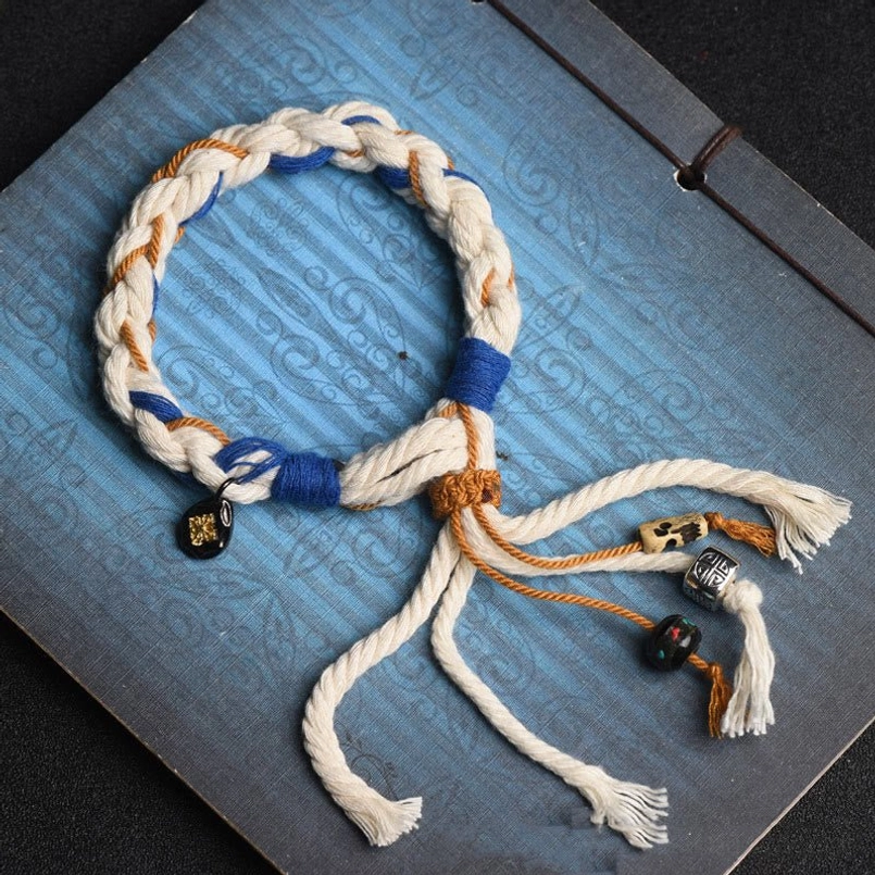Zakiram Goddess of Wealth red string bracelet with tri-color twisted rope and decorative copper pendants on blue vintage notebook