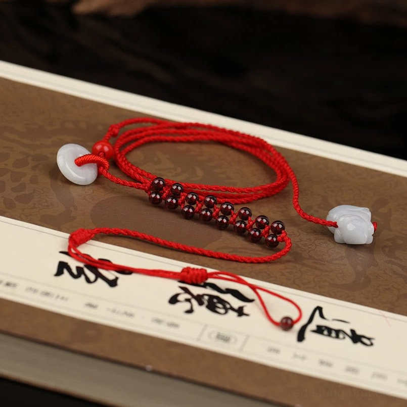 Red string belly chain with garnet stones and jade pendant displayed on Chinese calligraphy desktop