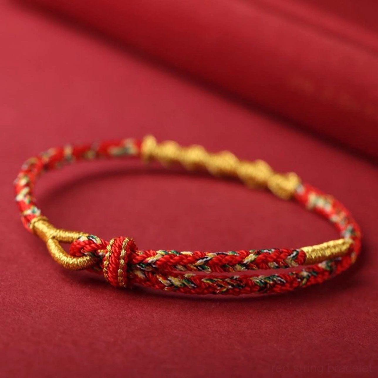 Flat lay view of handwoven red zodiac natal buddha protection bracelet with gold clasp