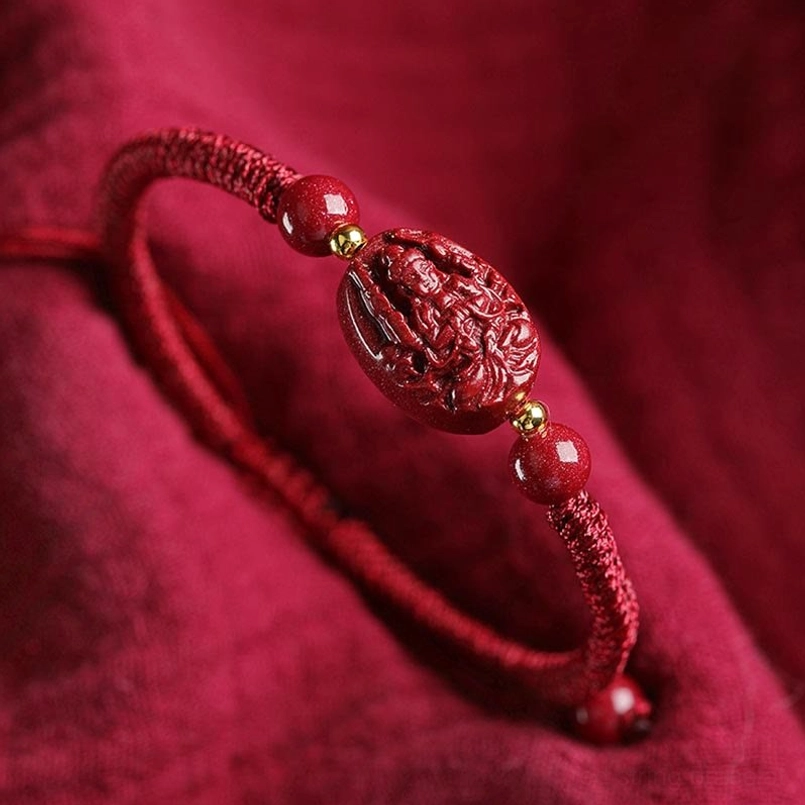 Close-up cinnabar natal buddha bracelet carved charm beaded accents dark fabric