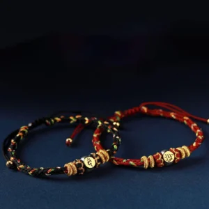 Chinese zodiac natal buddha red string bracelet with black and red woven cord, gold metal charm beads on dark background