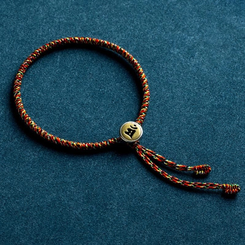 Close-up of single Chinese zodiac natal Buddha bracelet with tasseled rope ends and metal charm