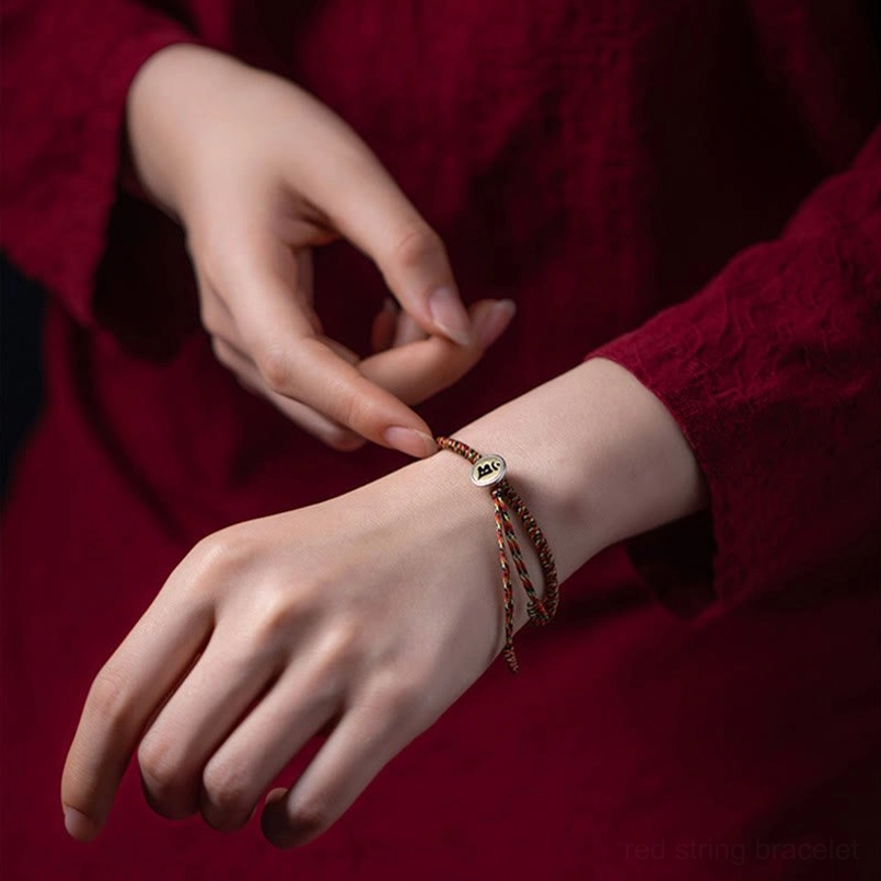 Person wearing Chinese zodiac natal Buddha protection bracelet on wrist with red fabric background