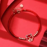 Chinese Zodiac Rat red string bracelet with sterling silver charm and gold beads on red fabric background