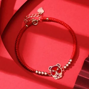 Chinese Zodiac Rat red string bracelet with sterling silver charm and gold beads on red fabric background
