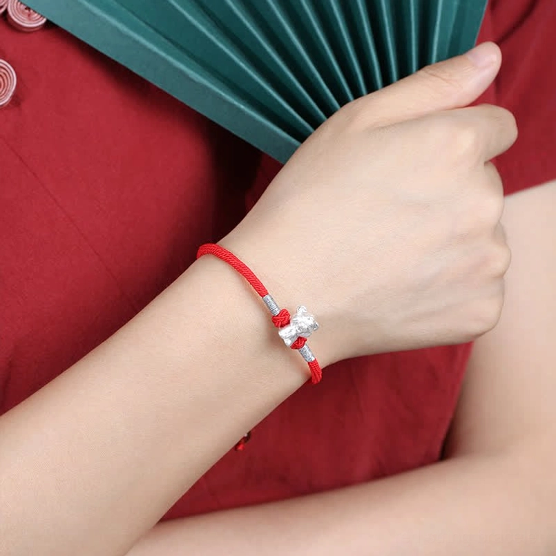 Red string zodiac bracelet worn on wrist with traditional Chinese cheongsam styling, close-up