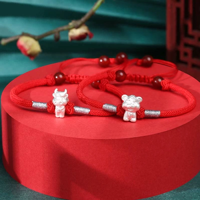 Two zodiac red string bracelets on red display stand with Chinese style decoration and silver charms