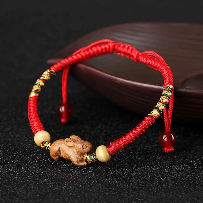 Chinese zodiac red string peach wood bracelet side view on wooden surface